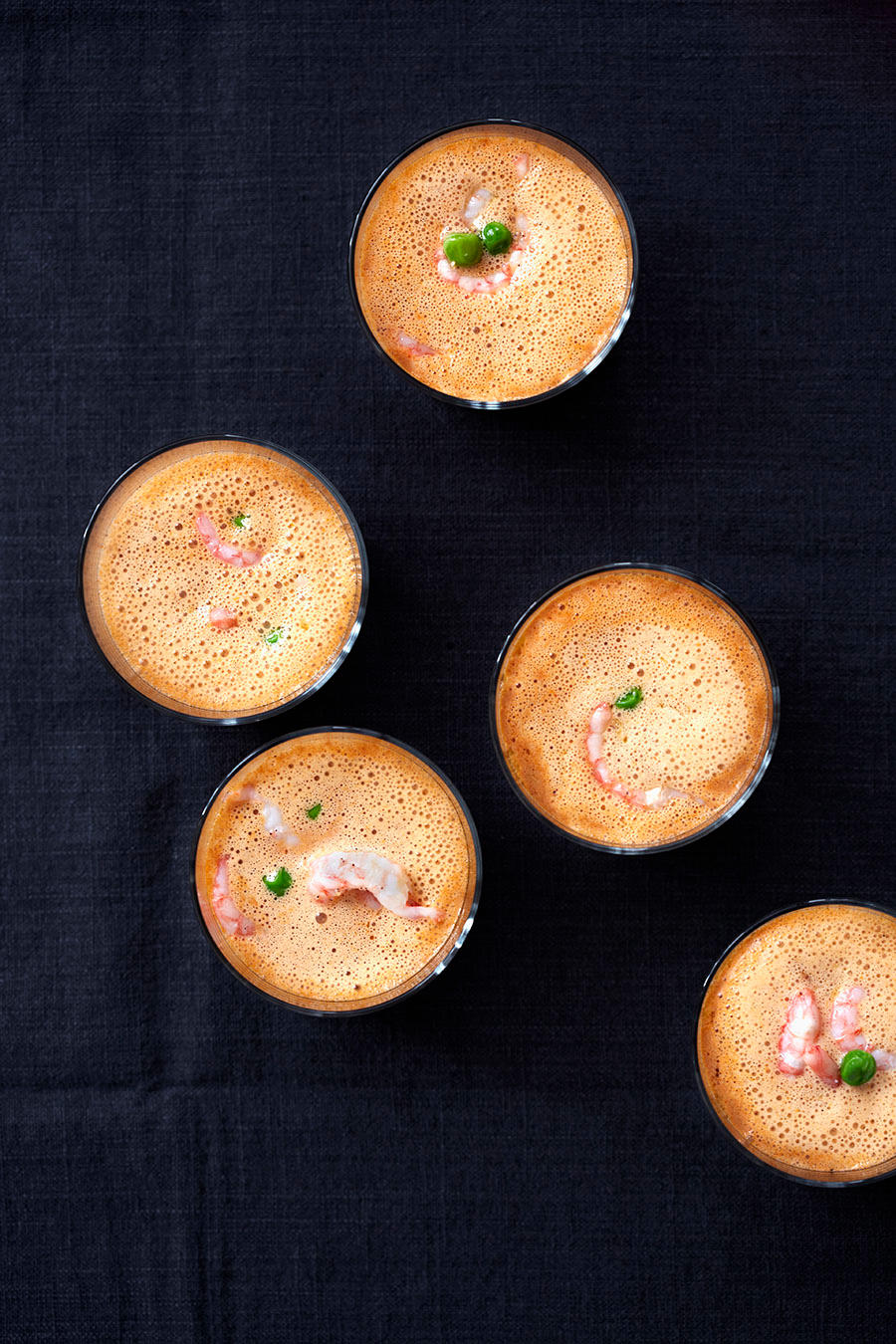 Små glass med rekesuppe med ferske reker og erter, servert på mørk duk.