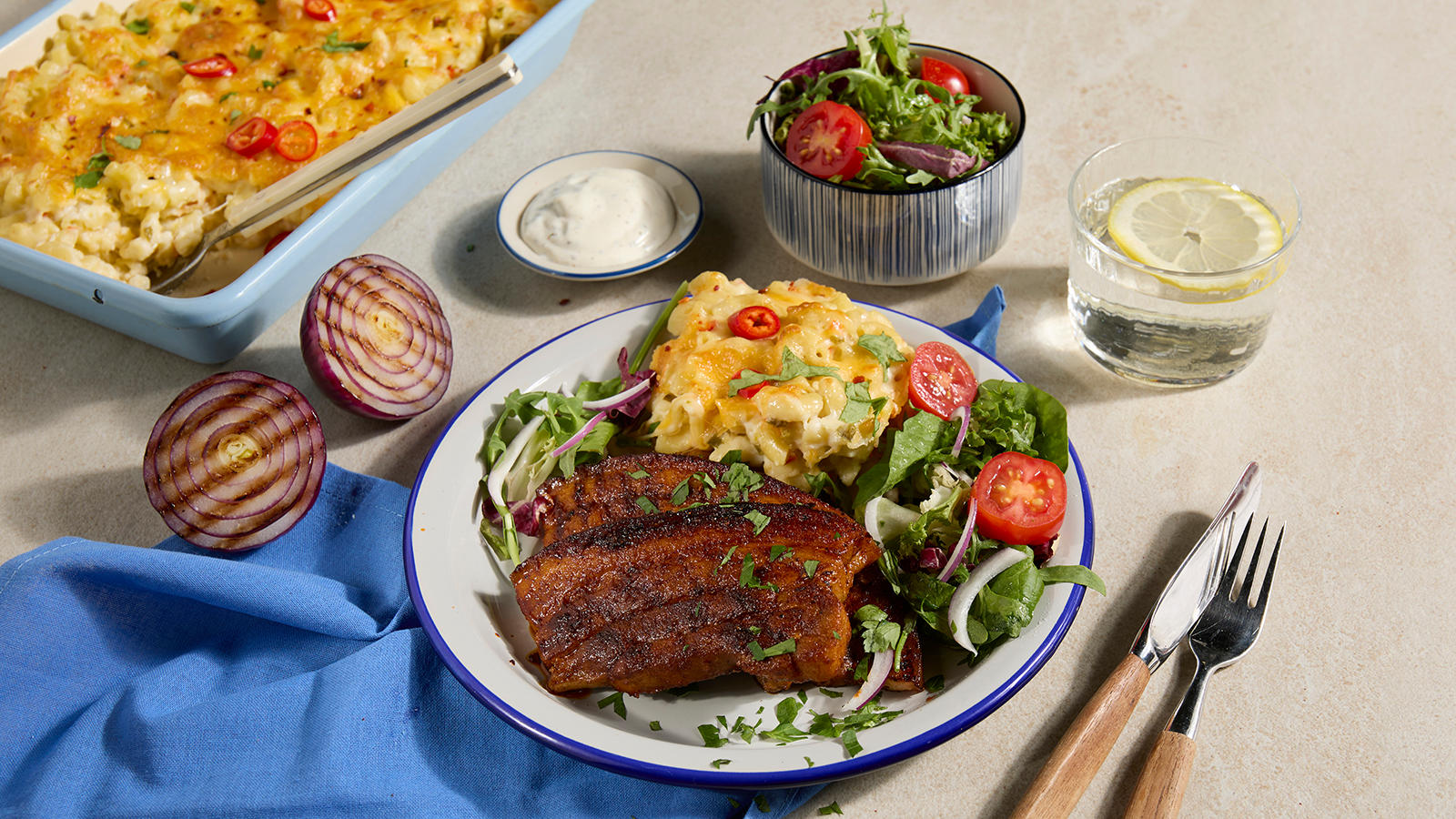 Grillribbe med jalapeno mac'n cheese servert på lys asjett med salat, tomater og rødløk. Form med mac'n cheese i bakgrunnen.