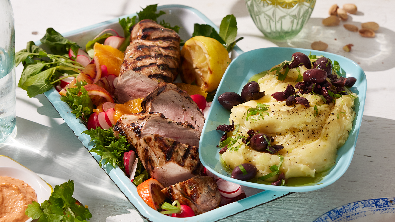 Indrefilet av svin med gresk potet- og hvitløksdipp servert med reddik, salat, oliven og appelsin i turkis form.