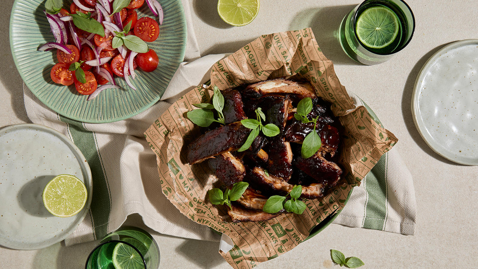 Spareribs med cola-glaze servert med et dryss frisk basilikum i Mega ferskvarepapir med en skål tomatsalat på siden.