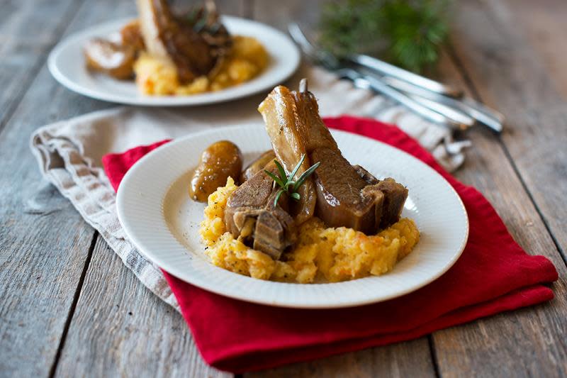 Pinnekjøtt servert på en seng av kålrabistappe, med poteter på siden og fersk rosmarin til pynt. Hvit tallerken, rød stoffserviett.