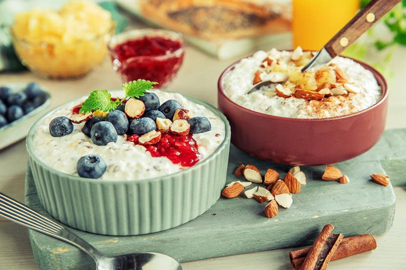To boller kjøleskapsgrøt i fargerike boller, med variert topping av bær, nøtter og syltetøy. Hyggelig frokostbord i bakgrunnen.