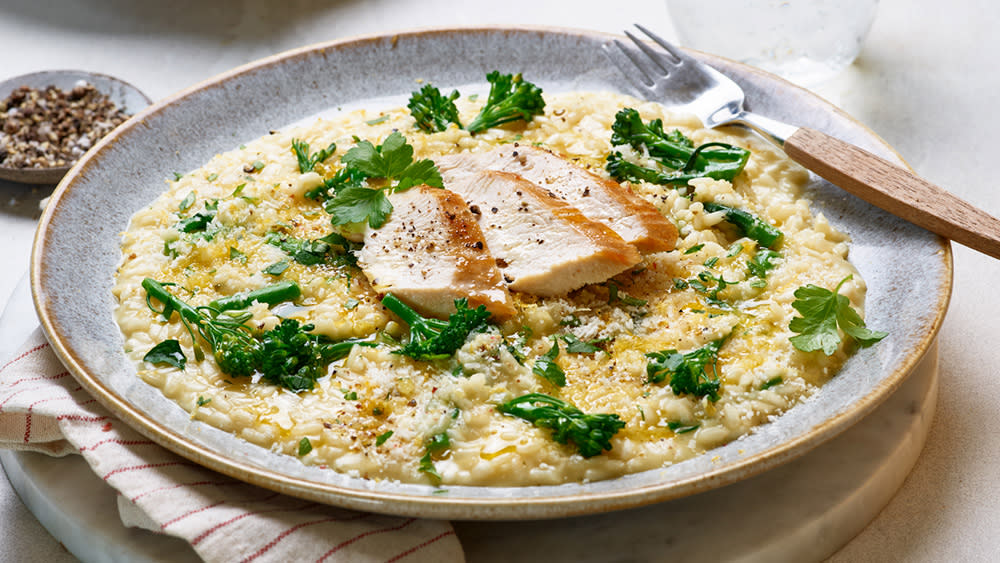 En tallerken med kremet risotto toppet med grønne brokkolibiter, urter og skiver av saftig kyllingbryst. Retten er dandert delikat med litt pepper på toppen.