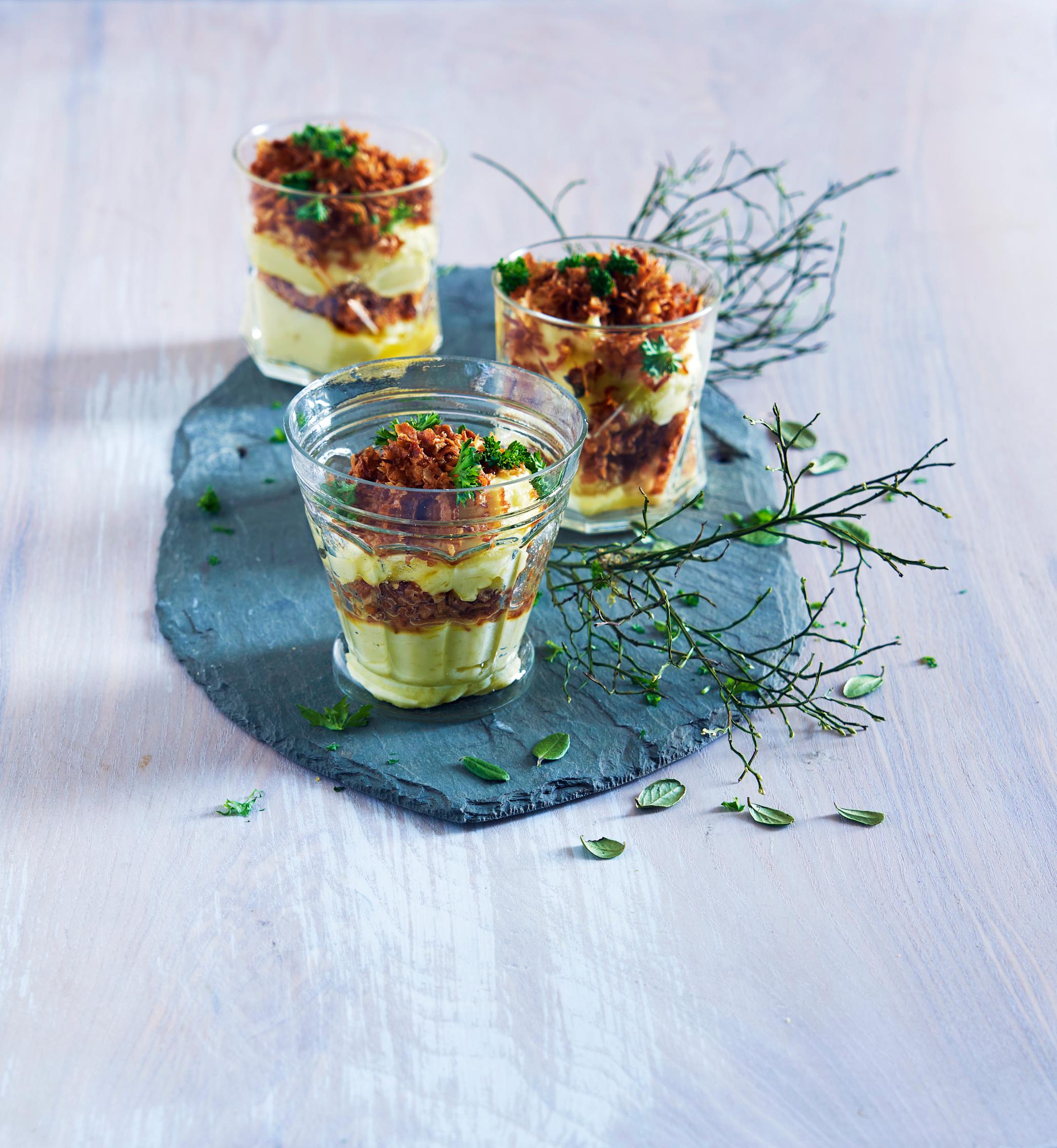 Myk potetpure med brunet smør, sprø løk og persille servert lagvis i glass på skiferhelle. Friske urter, og tynne grønne plantegrener strødd rundt.
