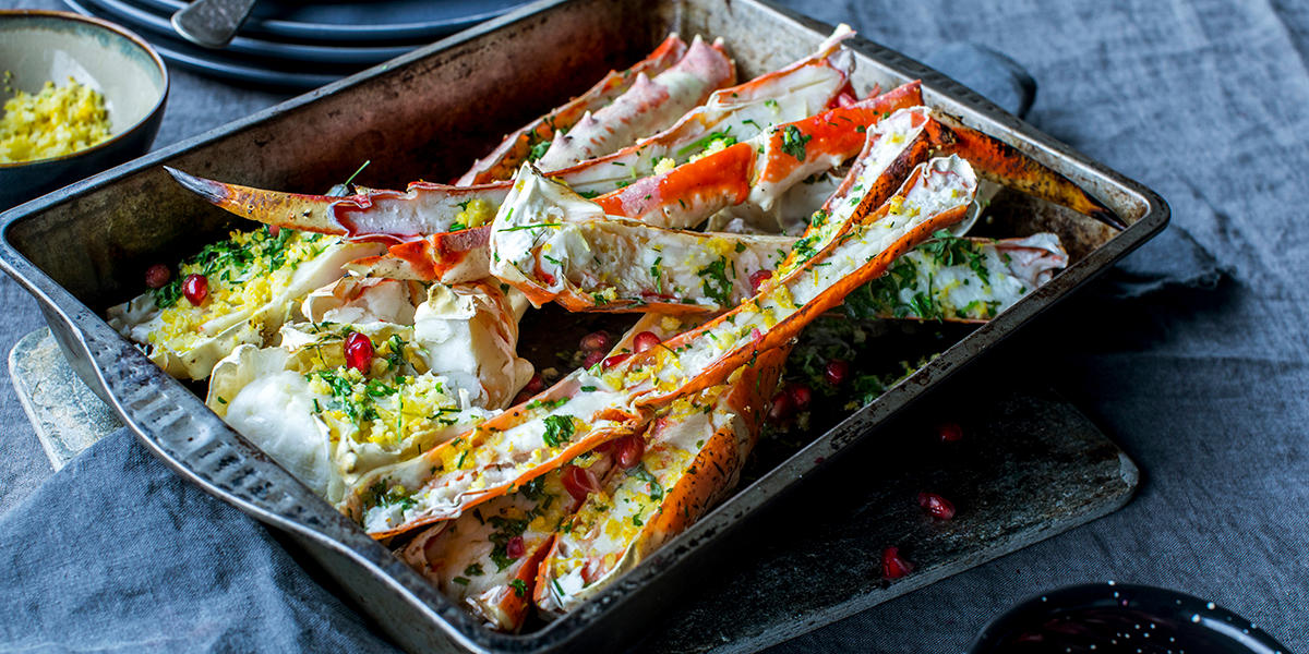 Gratinert bein av kongekrabbe med sitron, servert i metallform med sitronskall, urter og granateplefrø. Liten skål med revet sitronskall i bakgrunnen.