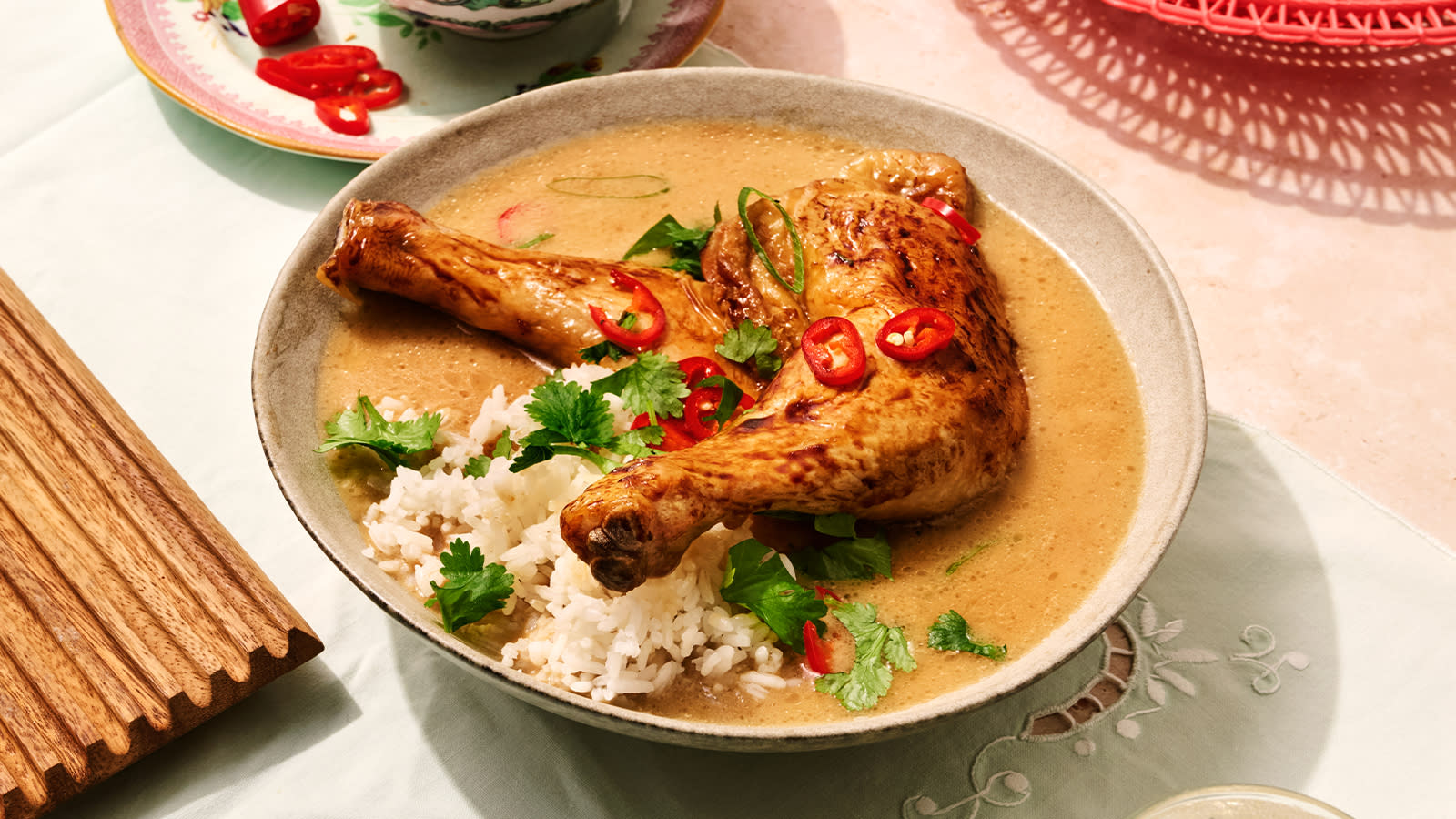 Kylling adobo med kokosmelk servert i dyp beige skål med adobosaus, ris, koriander og hakket rød chili.