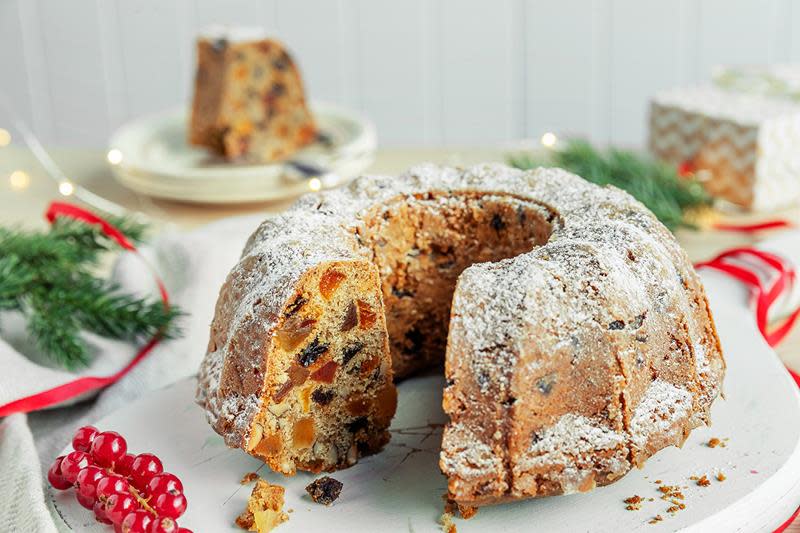 Gammeldags fruktkake med tørket frukt, servert på en hvit fjøl. Omringet av julelys, røde julebånd, grønt granbar og rød rips.