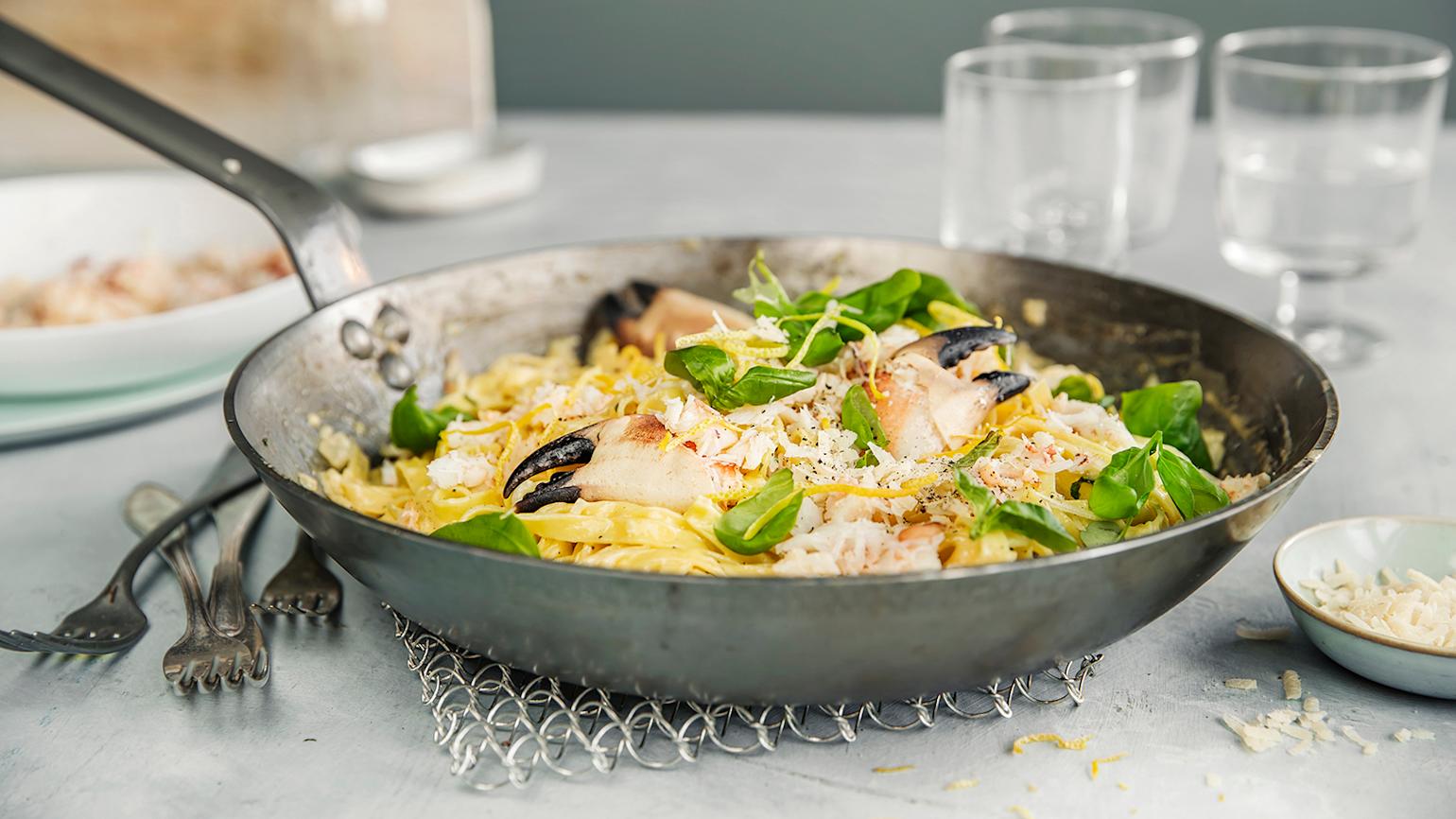 Kremet pasta med krabbe og frisk sitronsaus servert i metallpanne på dekket middagsbord.
