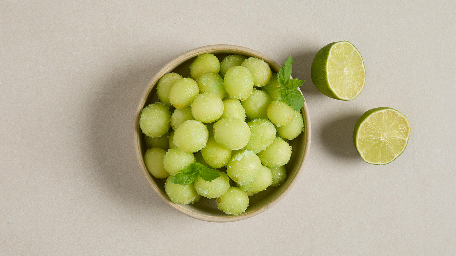 Frosne druer med gelépulver servert i lys skål og pyntet med noen blader frisk mynte. Frisk lime delt i to ved siden av.