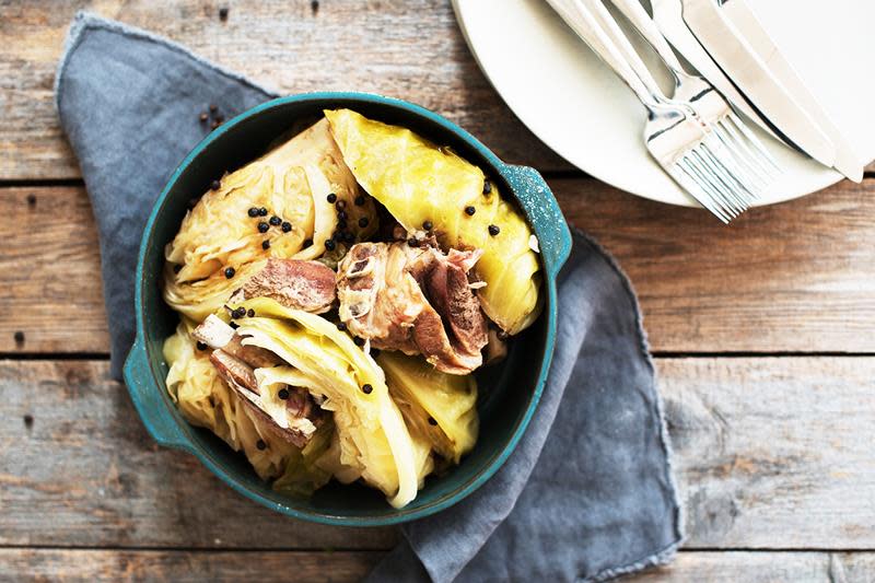 Tradisjonell fårikål med kål, lam og hel pepper servert i en turkis gryte på rustikk trebord. Mørkeblått kjøkkenhåndkle under, og bestikk ved siden av.