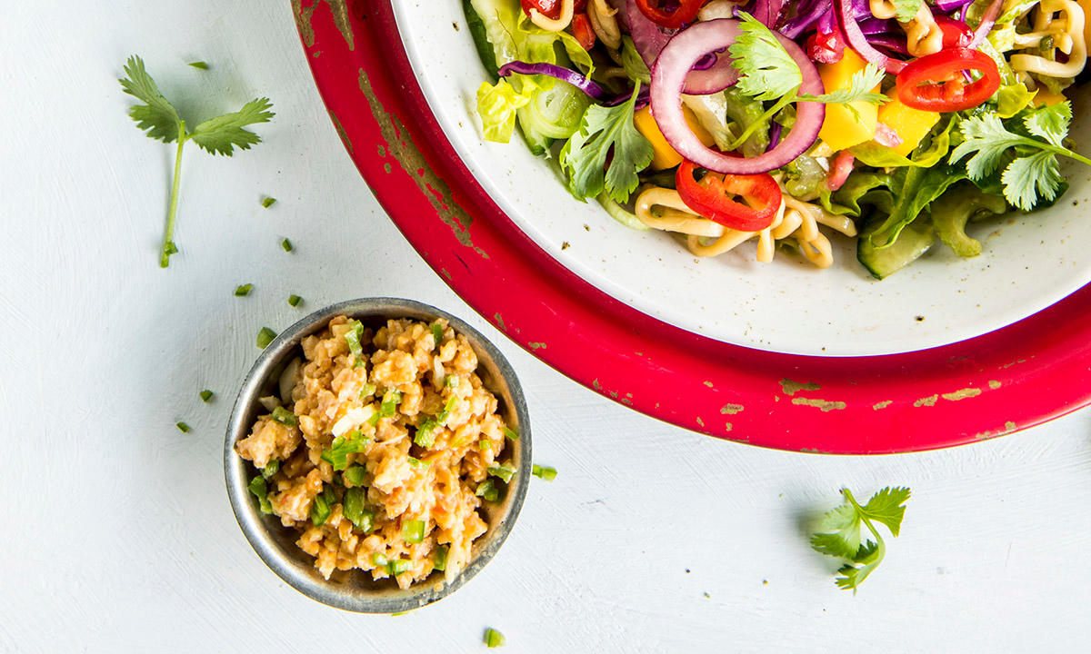 Asiatisk nudelsalat servert i en skål med rød kant, og peanøttkrem i en liten skål ved siden av.