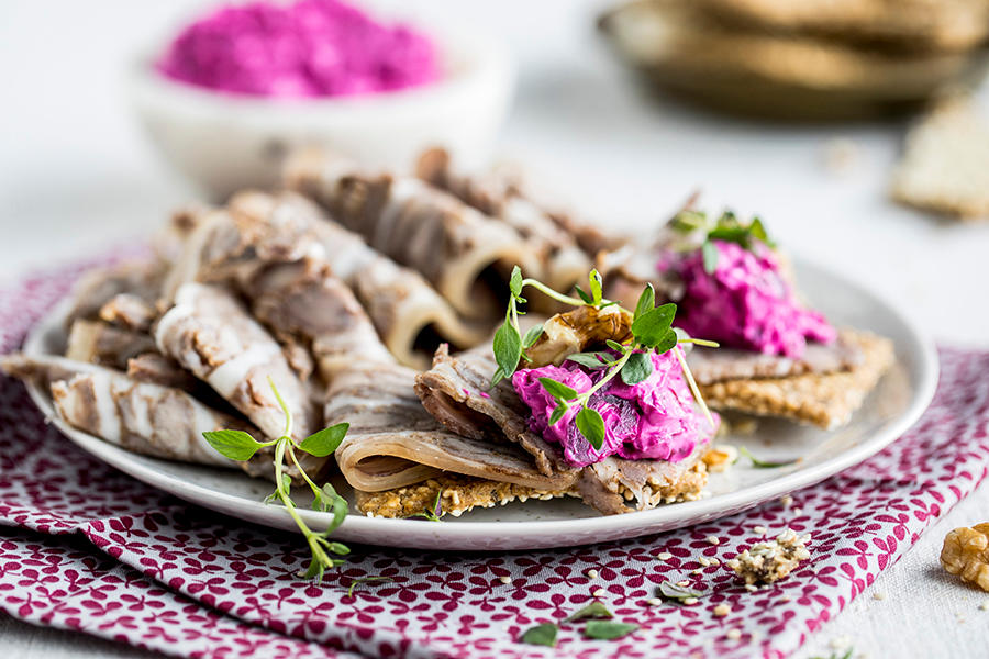 Sylte på knekkebrød med hjemmelaget rødbetekrem, servert på hvit tallerken og pyntet med fersk timian og valnøtter. Hvit skål med hjemmelaget rødbetekrem i bakgrunnen.