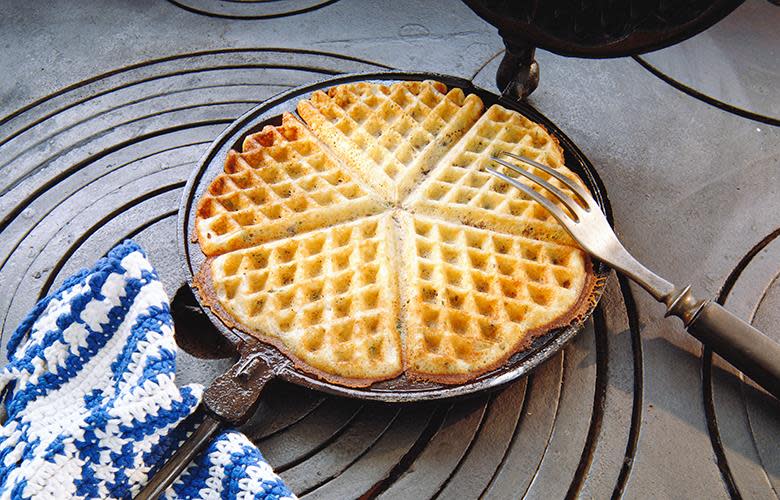 En nystekt gylden vaffelplate ligger i et tradisjonelt vaffeljern av støpejern.