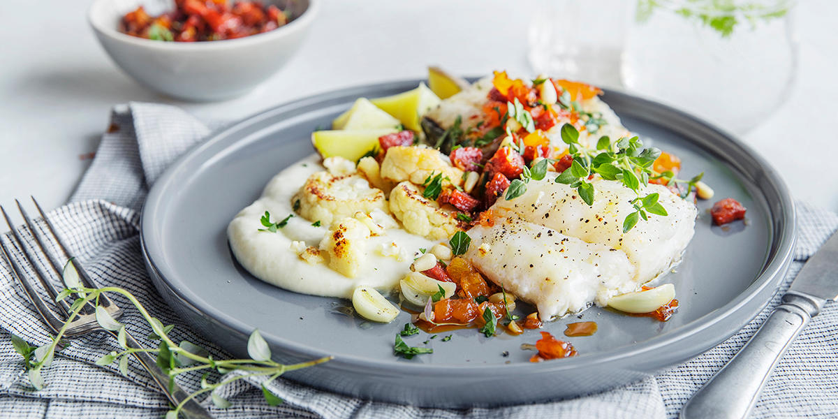 Stekt torsk med spenstig chorizosalsa og blomkålpuré, servert på grå tallerken med stekt blomkål og ferske urter på dekket middagsbord.
