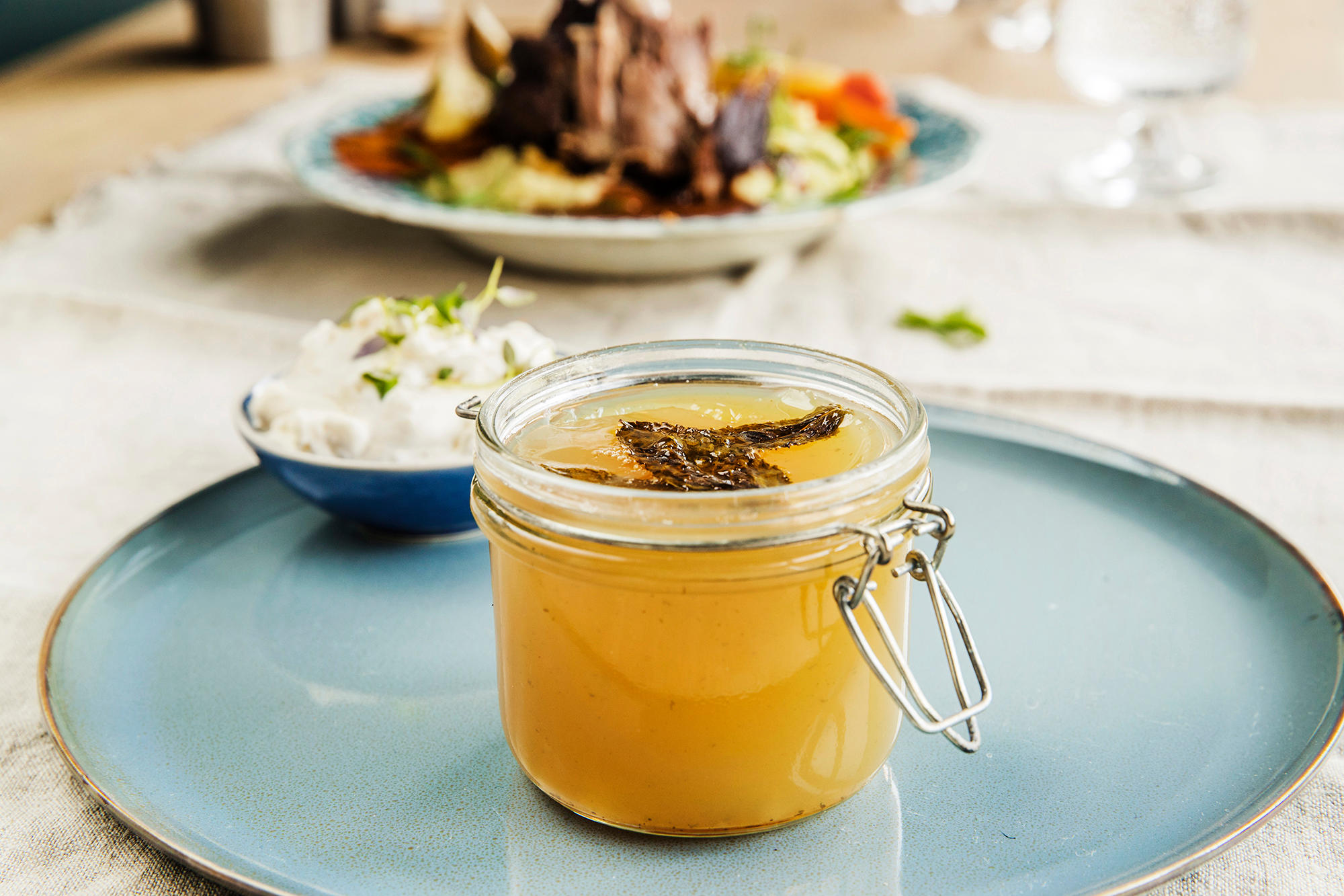 Hjemmelaget myntegele i åpent Norgesglass, servert på blå tallerken på lindukkledd middagsbord. Tallerken med braisert lammeskank i bakgrunnen.
