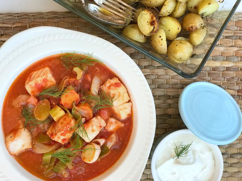 Tomatisert fiskegryte, med både rød og hvit fisk. Servert i hvit skål, toppet med dill, og med ovnsbakte poteter ved siden av.