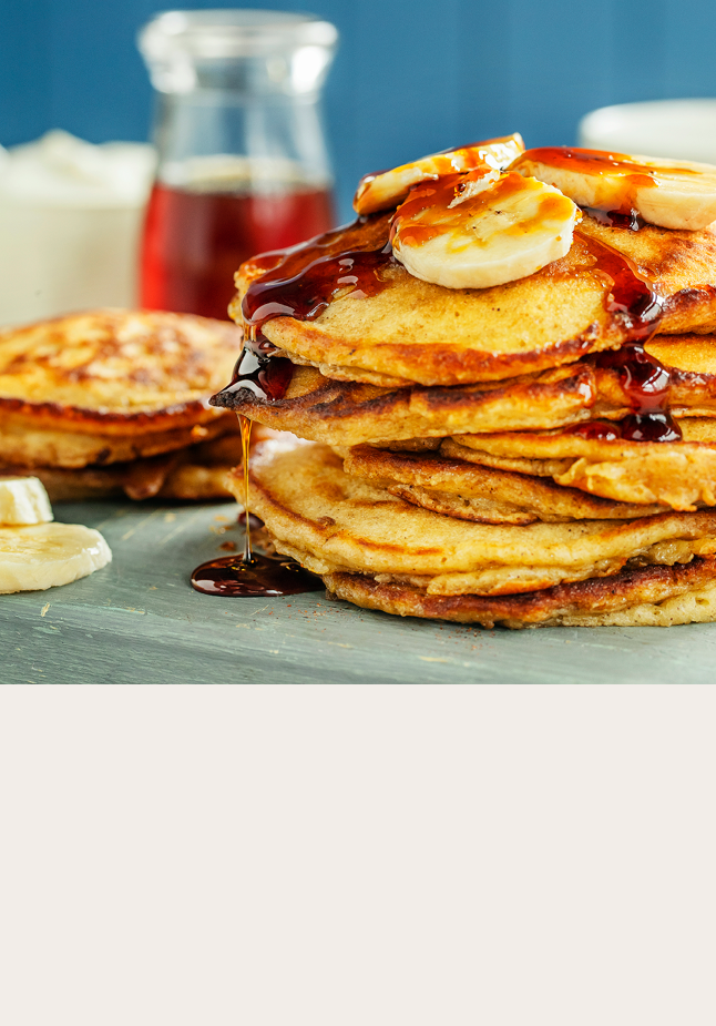 Et tårn med bananpannekaker med bananer i skiver på toppen og sirup som renner ned. 