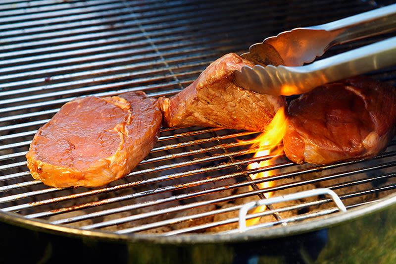 Krillklype som løfter et halvstekt stykke kjøtt fra grillen for å snu det over en flamme.