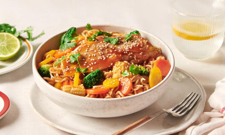 Lettsaltet torsk med asiatisk wok av grønnsaker og fullkornnudler med pad thai woksaus, servert i lys bolle på dekket middagsbord med vannglass med sitronskive ved siden av.