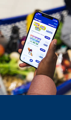 Mann holder mobil med Coop appen på skjermen i butikk