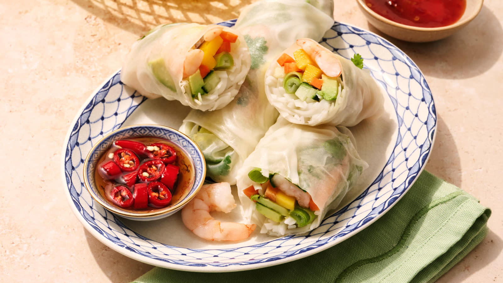 Vietnamesiske sommerruller med scampi og grønnsaker servert i hvit skål med blått mønster, med en skål dipsaus på siden.