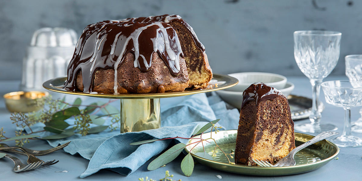 Saftig marmorkake med sjokoladeglasur og melisglasur, servert på gullfarget stettfat på dekket festbord.