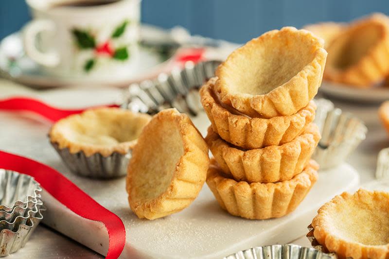 Klassiske sandkaker stablet i et tårn, omgitt av sandkakeformer, rødt julebånd og hyggelig juleservise.