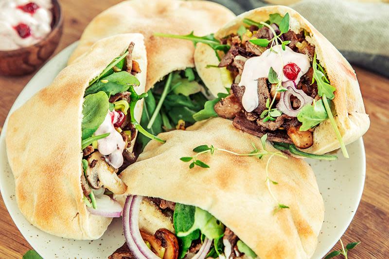 Reinskav i pita med tyttebærdressing, stekt sopp, rødløk, og salat servert på lys tallerken på rustikk trebord. Liten skål med tyttebærdressing i bakgrunnen.