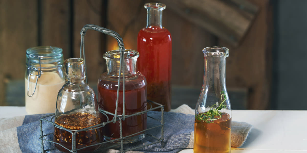 5 gode marinader til grillmaten, i flasker og krukker på bord.