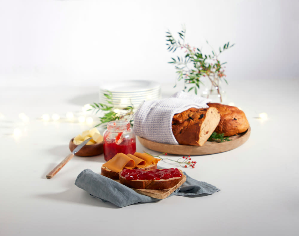 Vørterbrød i skiver med syltetøy og brunost, på liten trefjøl med grå serviett under. To vørterbrød i bakgrunnen med julelys bak.