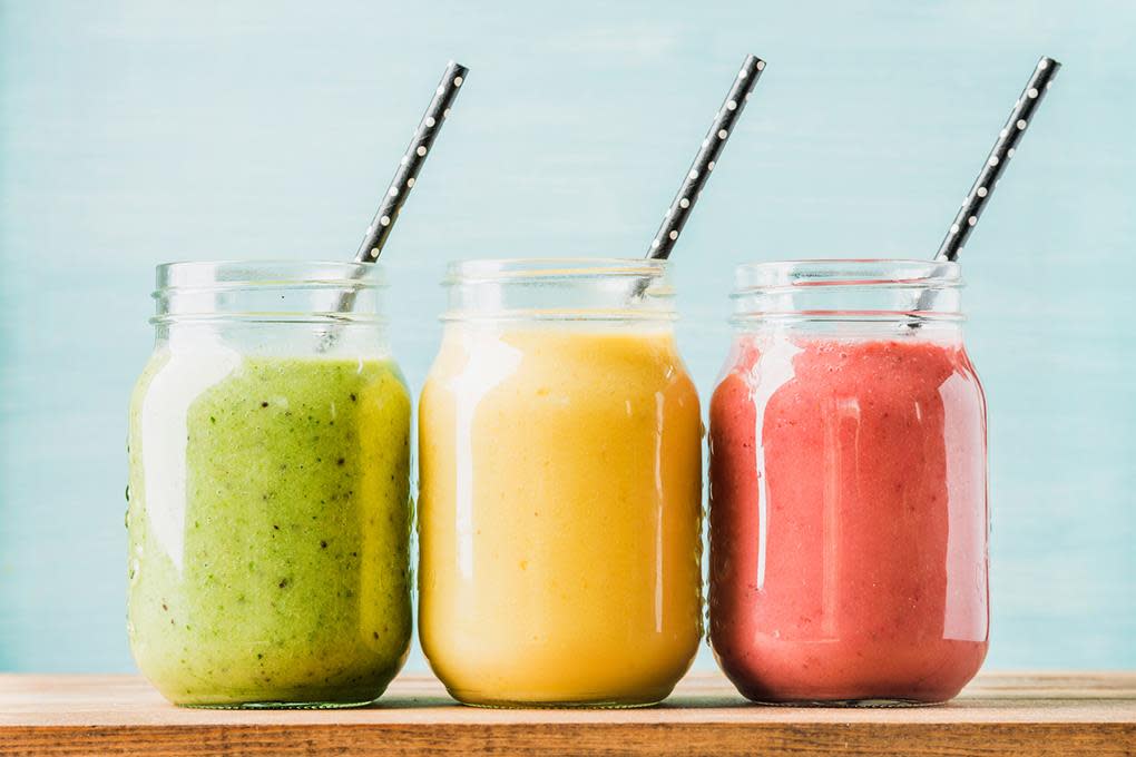 3 glass med fargerike smoothies ved siden av hverandre. Sugerør i hvert glass. Blå bakgrunn.