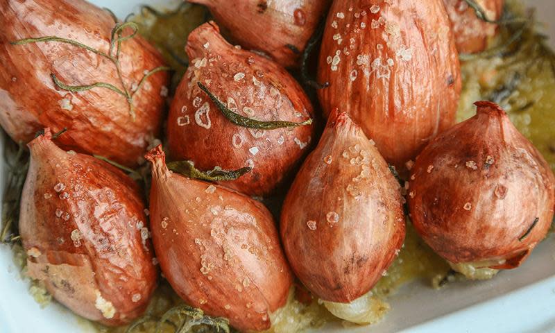 Saltbakt sjalottløk med skall, drysset med salt og rosmarin, ligger i en hvit ildfast form.