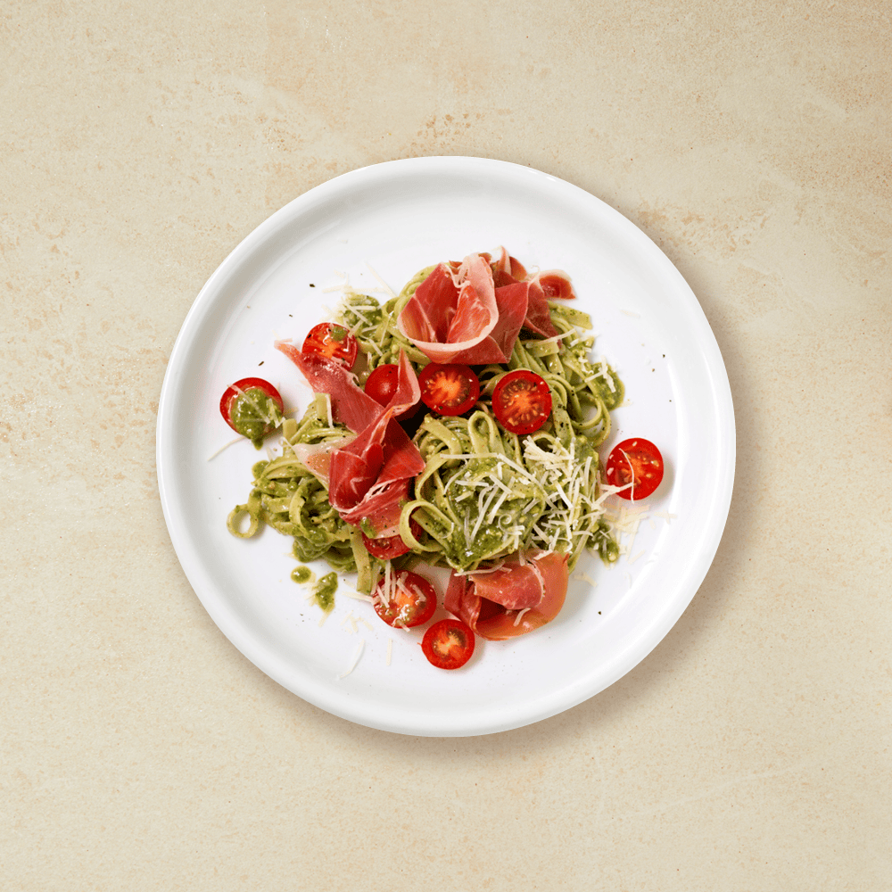 Pasta med pesto, skinke, tomat og parmesan på en hvit tallerken
