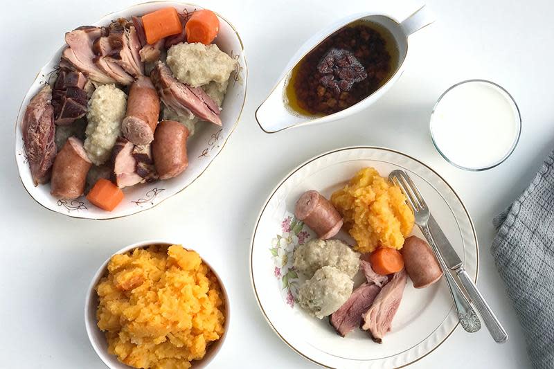 Dekket bord med raspeballer, kålrabistappe, bacon og kjøtt. Lys bakgrunn.