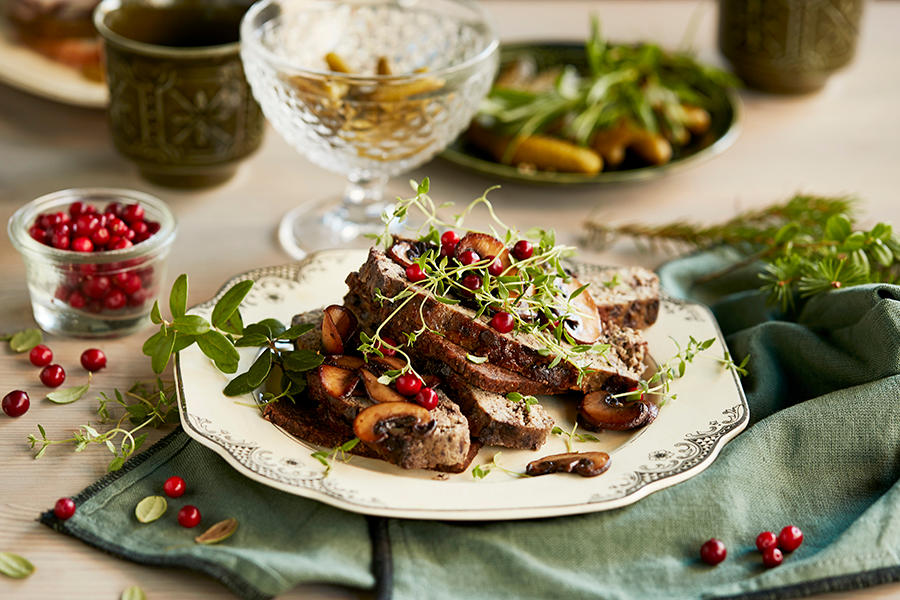 Hjemmelaget leverpostei med grønn pepper servert i skiver på hvit tallerken på dekket julebord. Leverposteien er pyntet med ferske tyttebær, stekt sopp og friske urter.