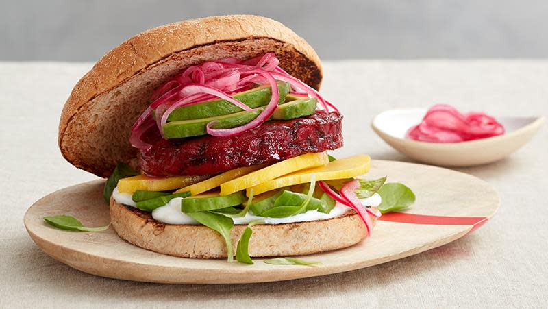Vegetarburger laget av rødbeter, med fetakrem og syltet rødløk, mango, avokado og babyspinat. Lys bakgrunn.