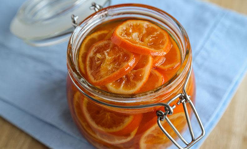 Fargesterke syltede klementiner i skiver, lagt på Norgesglass. Lys trebakgrunn med lyst blått kjøkkenhåndkle.