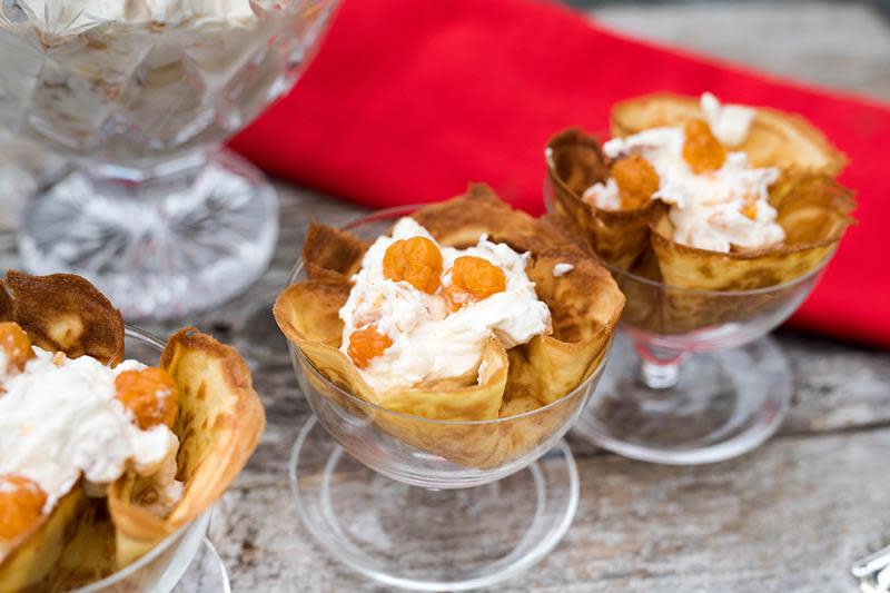 Klassisk multekrem servert i krumkakeskåler stående i dessertglass, og pyntet med multer på toppen. Rød serviett i bakgrunnen.