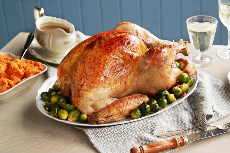 Helstekt kalkun med gyldent skinn servert på fat med rosenkål. Sausenebb med saus ved siden av. Pent dekket bord.