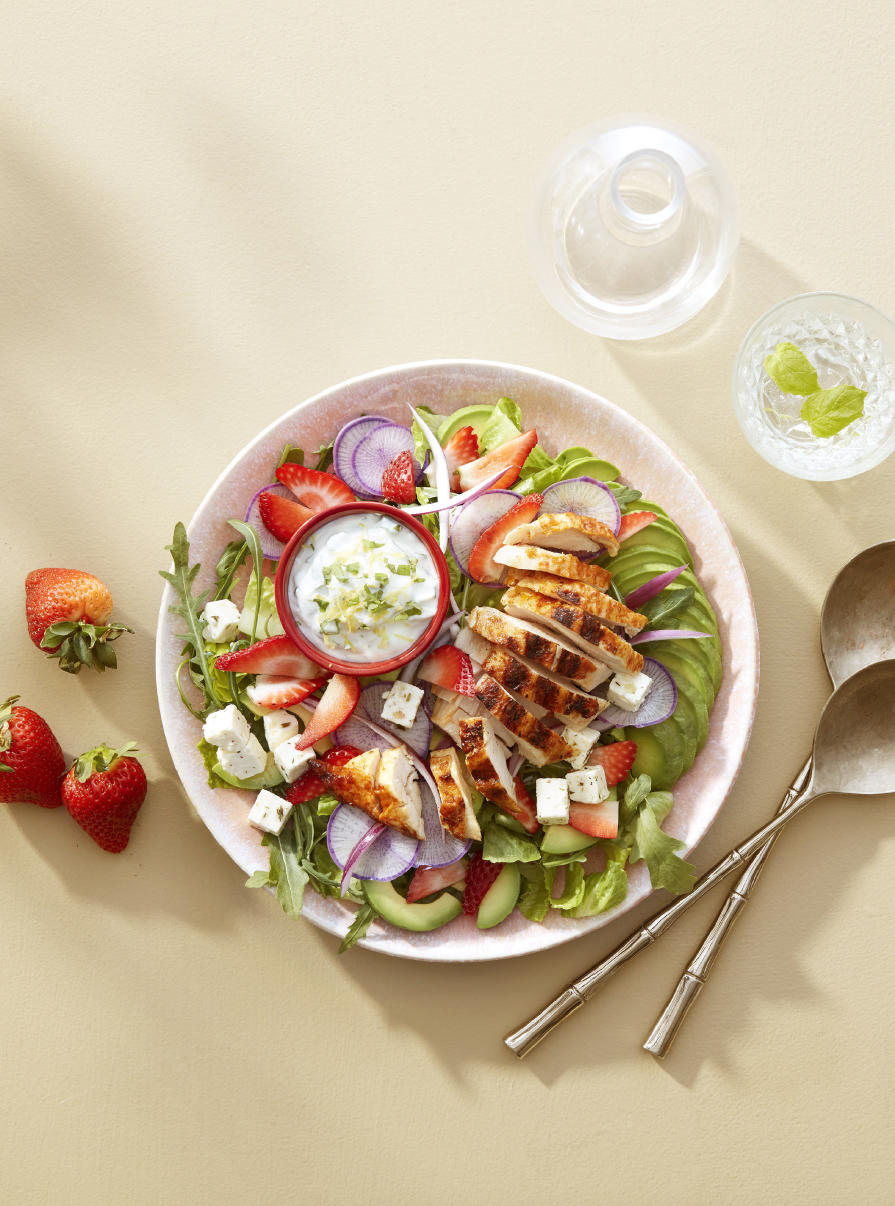 Sommerlig kyllingsalat med hjemmelaget urtedressing servert i lys skål med avokado, rødløk, reddik, jordbær og fetaost. Salatbestikk og friske hele jordbær på siden.
