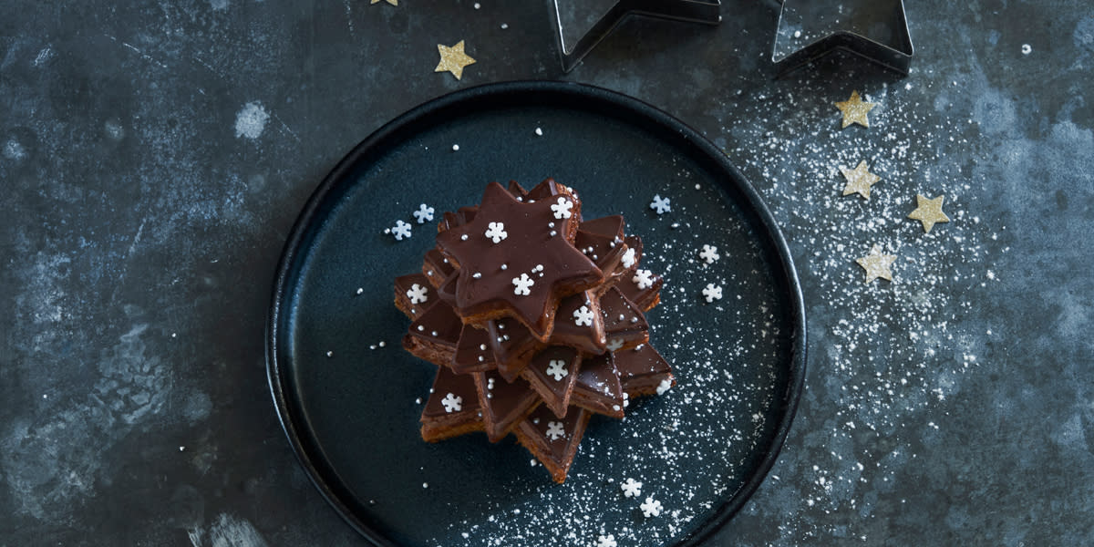 Konfektkaken Sarah Bernard stukket ut i form av stjerner og stablet oppå hverandre for å skape et juletre. Juletreet er pyntet med litt melis, og kakepynt i form av hvite snøfnugg, og er servert på en mørk tallerken på mørk bakrunn med små gullstjerner.