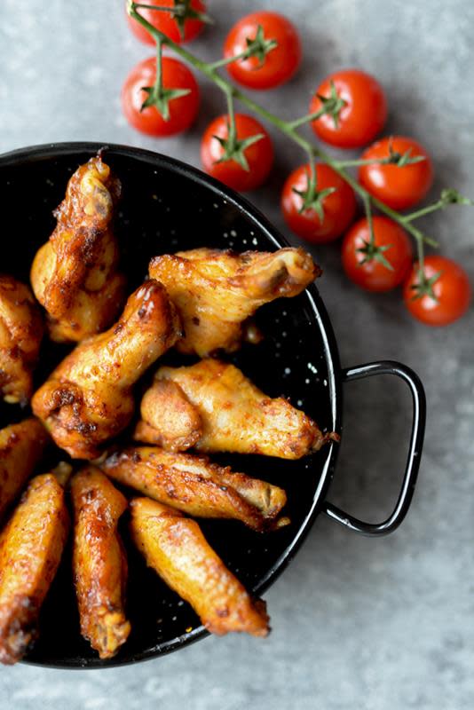 Kyllingklubber til tapas i svart serveringsform på grå bakgrunn. Klase med småtomater ved siden av.