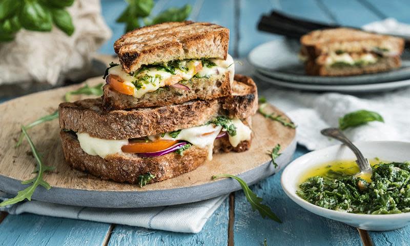 Caprese ostesmørbrød med ruccolapesto, oransje tomater, mozzarello og aioli på trefjøl. Ekstra ruccolapesto i skål ved siden av.