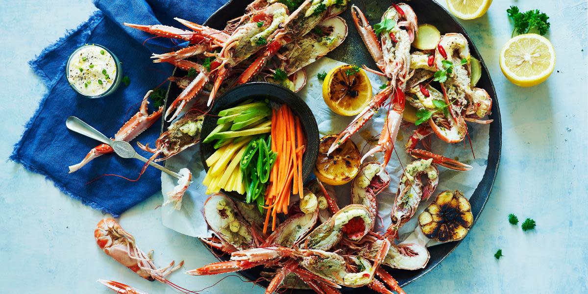 Gratinert sjøkreps på mørkt fat med grillet sitron og finsnittede grønnsaker i skål. Mørkeblå linserviett på siden.