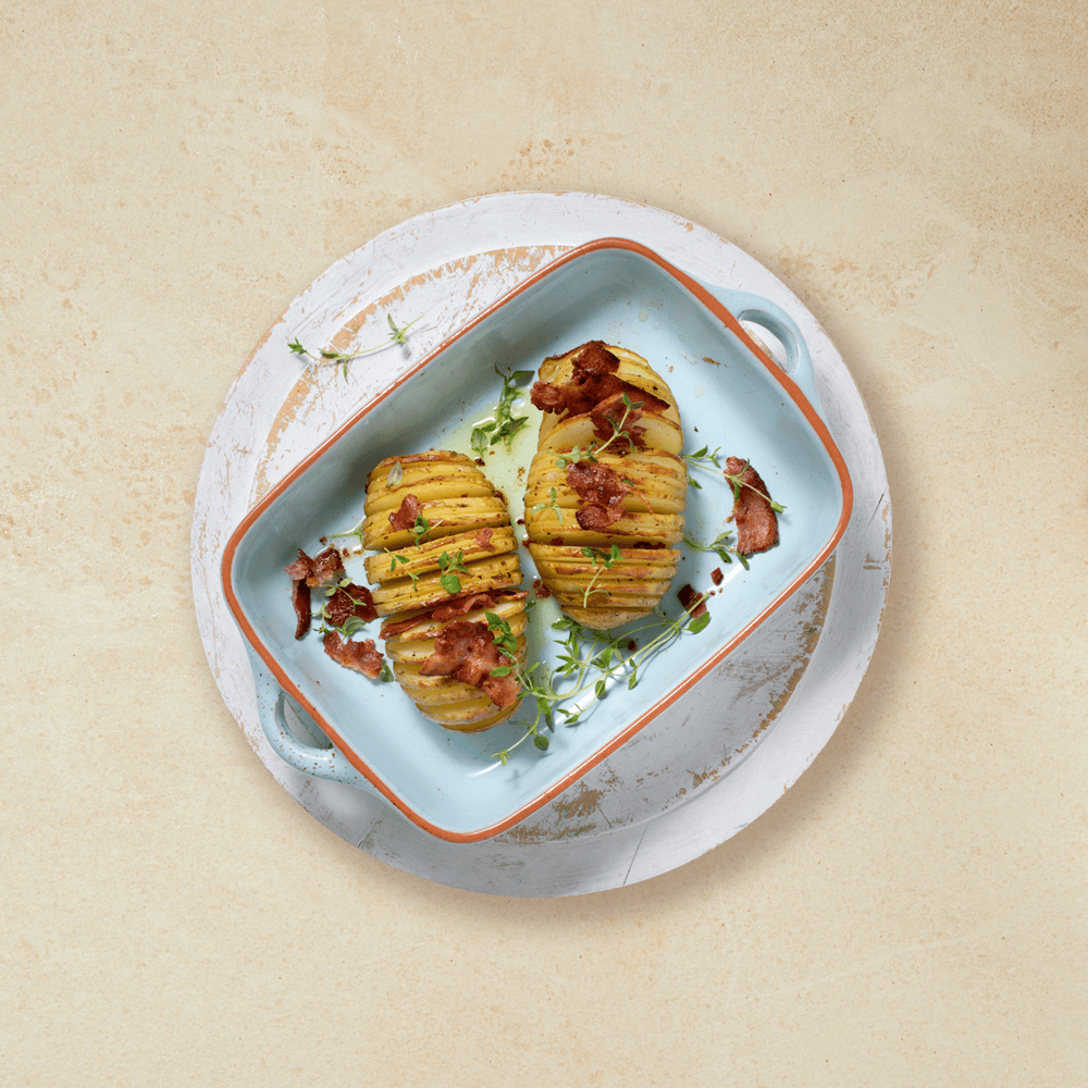 Hasselbackpoteter toppet med bacon, i en lys blå ildfast form med rød kant.