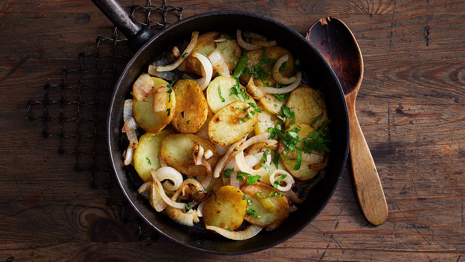 Pommes lyonnaise – sprøstekte poteter med løk servert i mørk støpejernspanne på rustikk trebord.