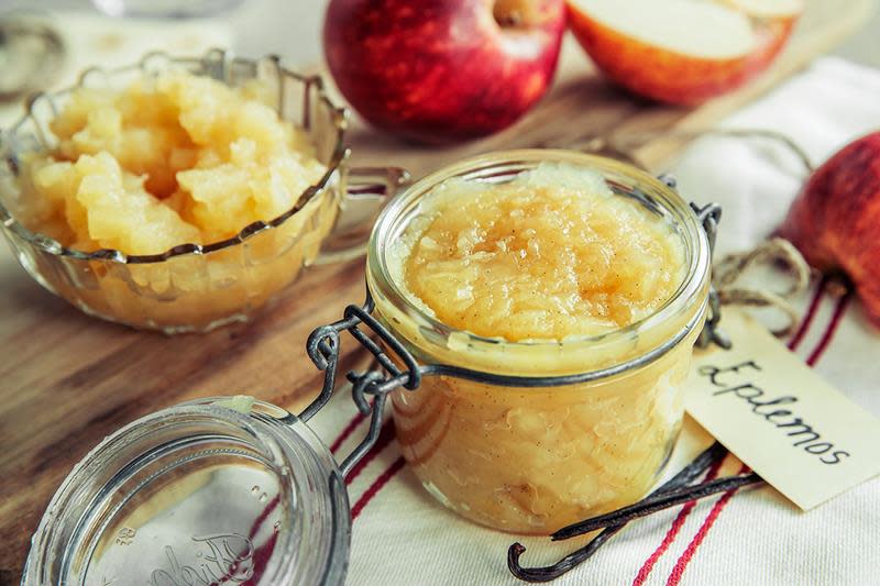 Hjemmelaget eplemos på syltetøyglass, hyggelig linduk med striper ved siden av. Røde epler og vaniljestenger.