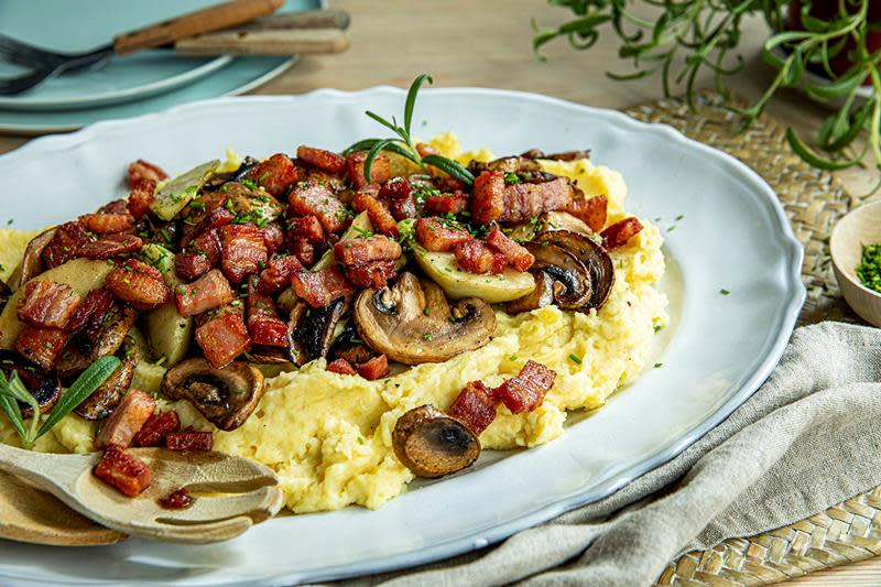 Brennende kjærlighet; potetmos med sprøstekt bacon og sopp, servert på ovalt hvitt fat på dekket middagsbord med ferske urter.