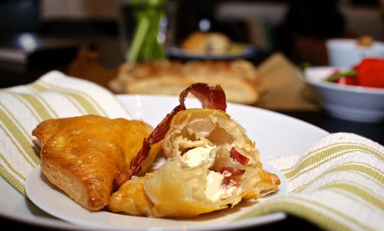 Samosas med kremost og bacon, delt i to og lagt på hvit tallerken med grønnstripet serviett.