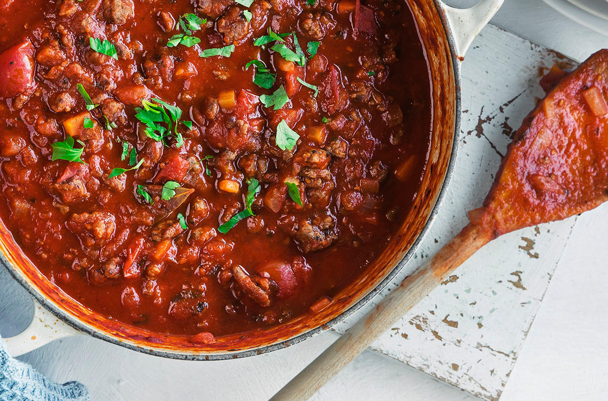 Pastasaus i kjele pyntet med hakket persille ved siden av en tresleiv som har blitt brukt til røring.